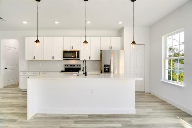 kitchen with white cabinetry, appliances with stainless steel finishes, hanging light fixtures, and a kitchen island with sink