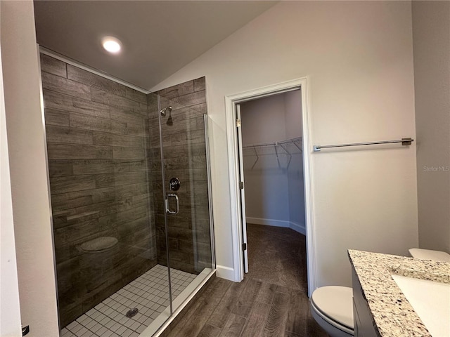 bathroom featuring hardwood / wood-style floors, vanity, a shower with door, vaulted ceiling, and toilet