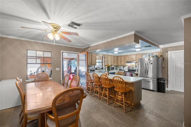 tiled dining room featuring ceiling fan, plenty of natural light, a textured ceiling, and ornamental molding