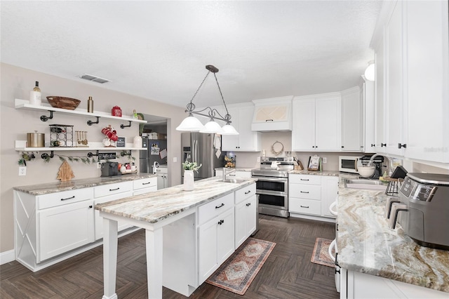 kitchen featuring decorative light fixtures, white cabinets, stainless steel appliances, and a kitchen island with sink