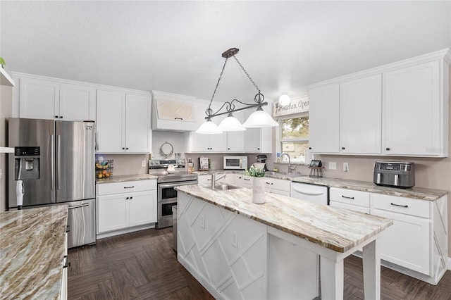 kitchen featuring white cabinets, a kitchen island, light stone countertops, appliances with stainless steel finishes, and decorative light fixtures