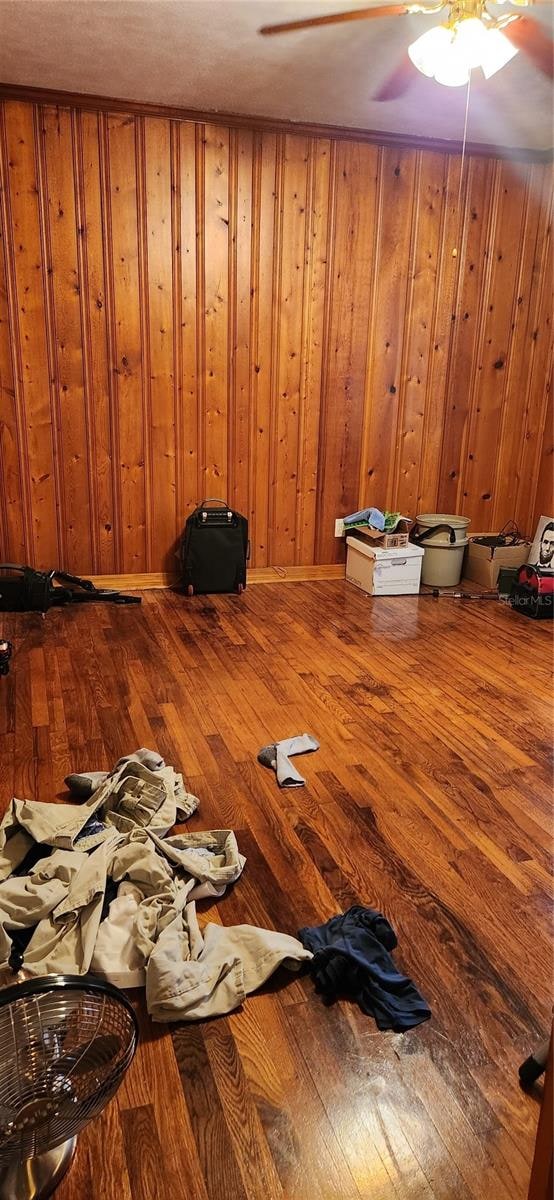 interior space with wood walls, hardwood / wood-style flooring, and ceiling fan