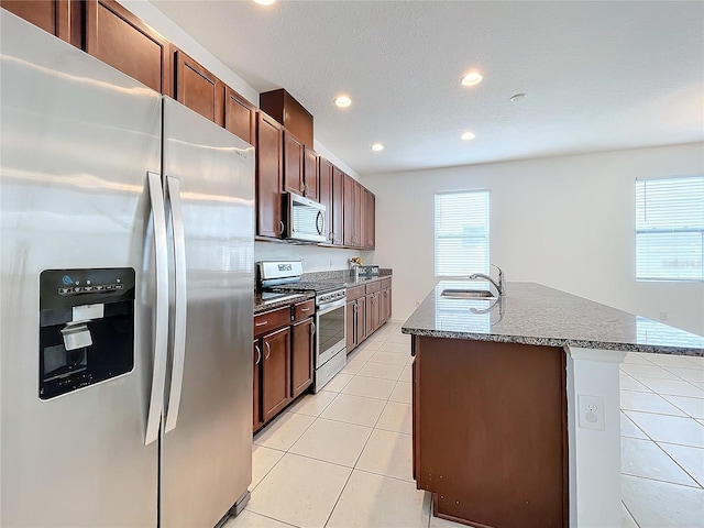 kitchen with a textured ceiling, stainless steel appliances, a kitchen island with sink, sink, and light tile patterned floors