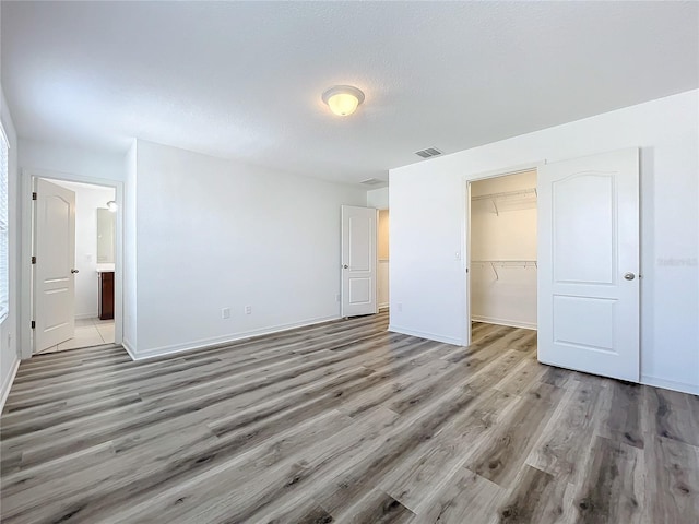 unfurnished bedroom featuring connected bathroom, a spacious closet, a closet, and light hardwood / wood-style floors