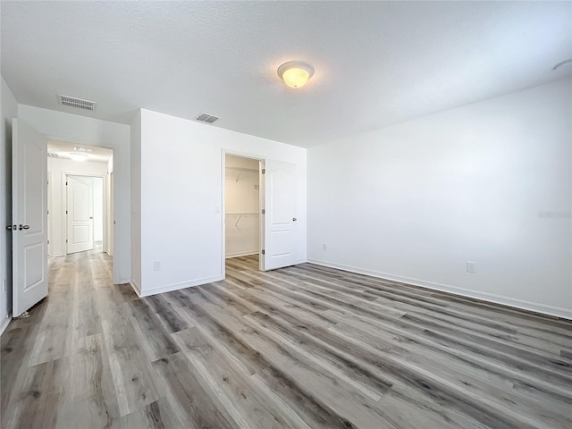 unfurnished bedroom featuring a textured ceiling, a walk in closet, light hardwood / wood-style floors, and a closet