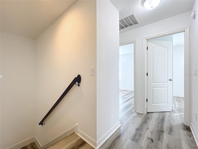 hall with a textured ceiling and light hardwood / wood-style flooring