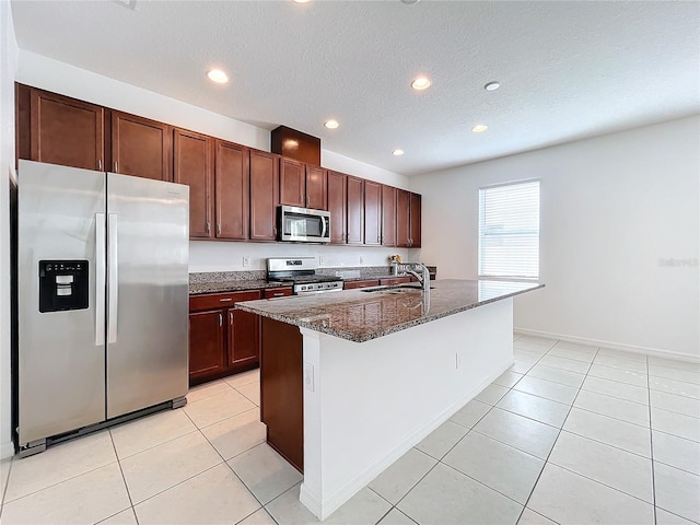 kitchen with a kitchen island with sink, dark stone counters, sink, a textured ceiling, and appliances with stainless steel finishes