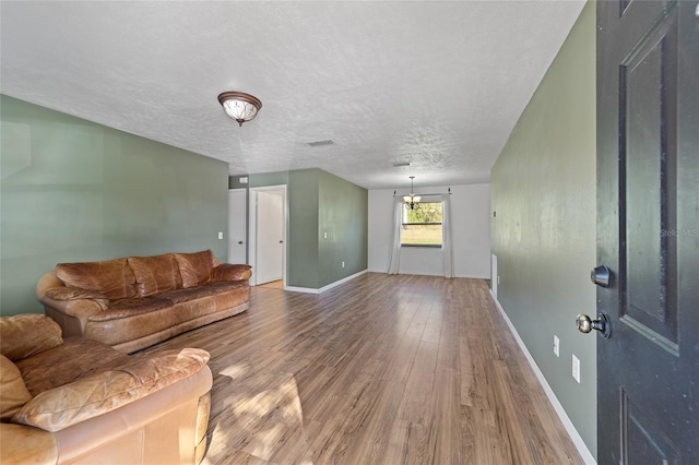 living room featuring wood finished floors, visible vents, baseboards, a textured ceiling, and a chandelier