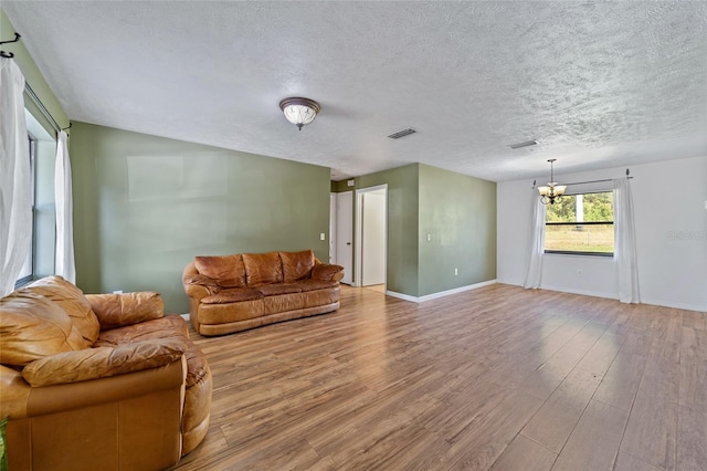 unfurnished living room with wood finished floors, baseboards, visible vents, a textured ceiling, and a chandelier