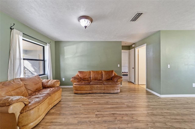 living area with a textured ceiling, wood finished floors, visible vents, and baseboards