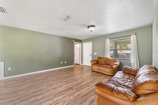 living room featuring a textured ceiling, baseboards, visible vents, and light wood-type flooring