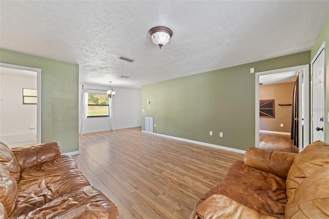 living area featuring light wood-type flooring, visible vents, a textured ceiling, and a chandelier