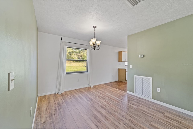 unfurnished dining area featuring visible vents, a textured ceiling, an inviting chandelier, and light wood finished floors