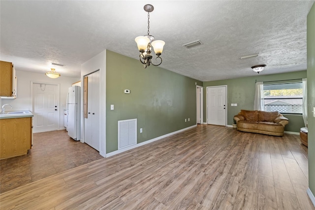 unfurnished living room featuring a sink, visible vents, a textured ceiling, and light wood finished floors