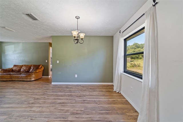 empty room featuring wood finished floors, baseboards, visible vents, an inviting chandelier, and a textured ceiling