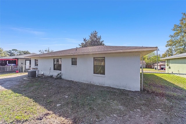 back of house featuring central air condition unit, fence, a lawn, and stucco siding