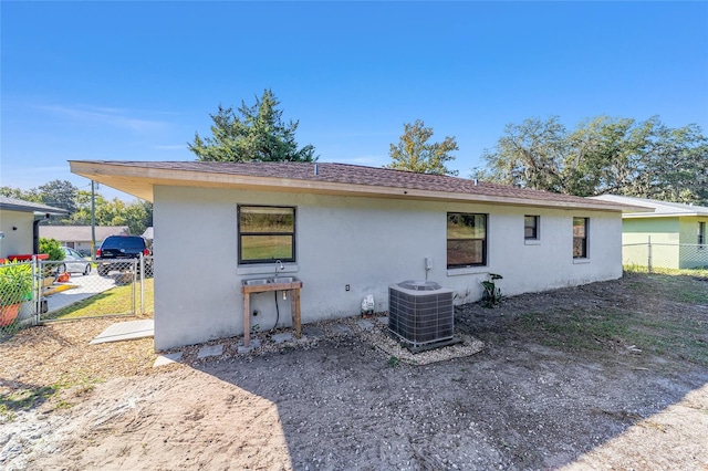 rear view of property with central air condition unit, stucco siding, and fence