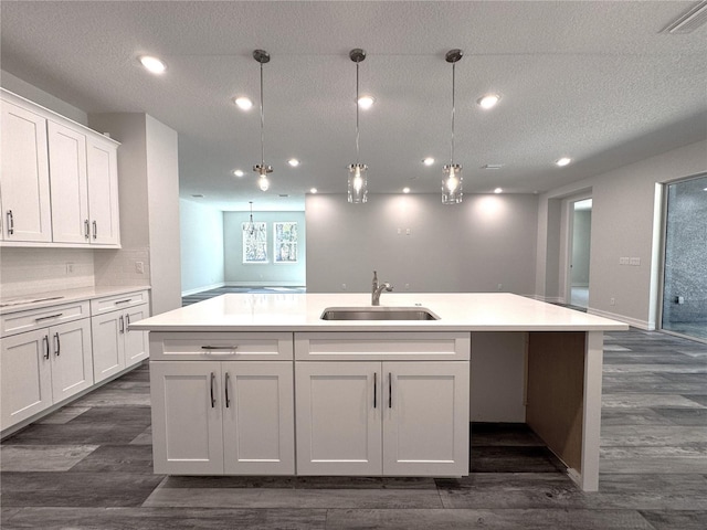 kitchen with a sink, visible vents, white cabinets, light countertops, and a center island with sink