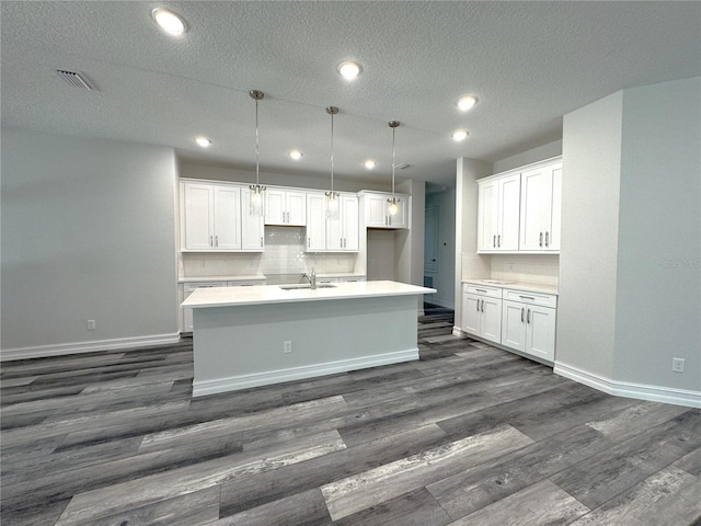 kitchen with dark wood-style flooring, a kitchen island with sink, a sink, white cabinetry, and baseboards