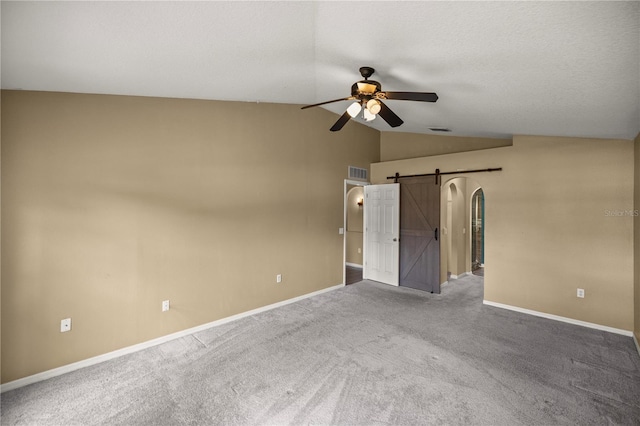 empty room featuring lofted ceiling, a barn door, ceiling fan, and carpet floors