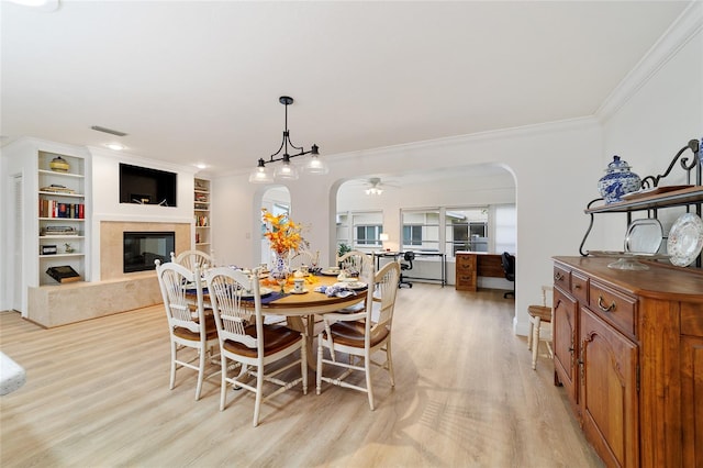 dining room with light hardwood / wood-style floors, built in shelves, ornamental molding, ceiling fan, and a premium fireplace