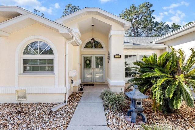 view of exterior entry featuring roof with shingles, visible vents, and stucco siding