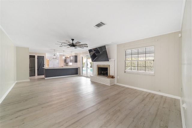 unfurnished living room with a fireplace, ceiling fan with notable chandelier, light wood-type flooring, and ornamental molding