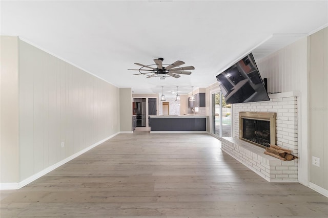 unfurnished living room featuring ornamental molding, ceiling fan, light hardwood / wood-style floors, and a brick fireplace