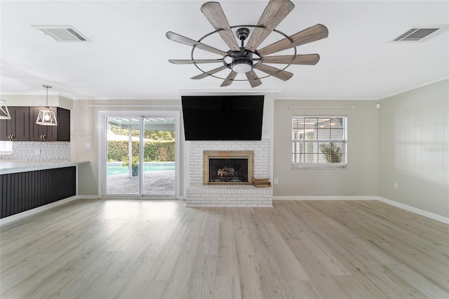 unfurnished living room featuring a brick fireplace, ceiling fan, light hardwood / wood-style flooring, and ornamental molding