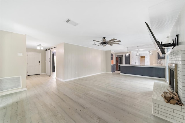 unfurnished living room with wooden walls, a barn door, ceiling fan, a fireplace, and light hardwood / wood-style flooring