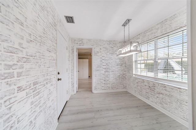 unfurnished dining area featuring light hardwood / wood-style floors and brick wall