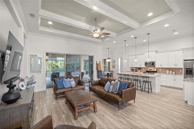 living room with beam ceiling, ceiling fan, ornamental molding, and light wood-type flooring