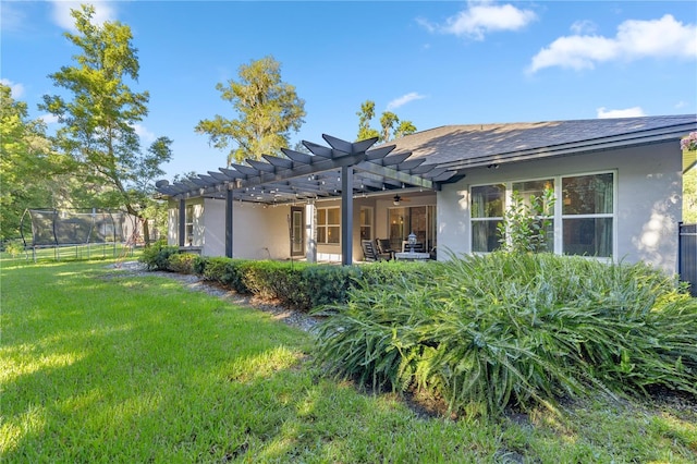 rear view of property featuring a pergola, ceiling fan, a lawn, and a trampoline