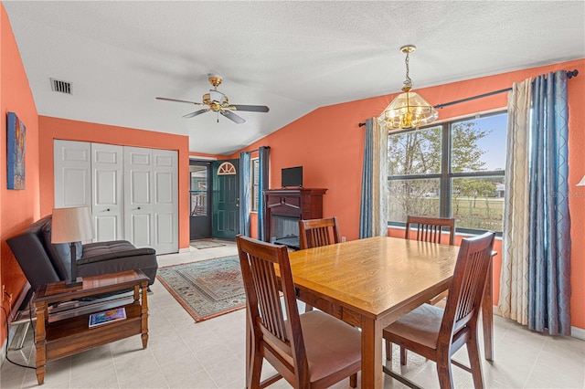 dining space featuring ceiling fan with notable chandelier, lofted ceiling, a textured ceiling, and light tile patterned flooring