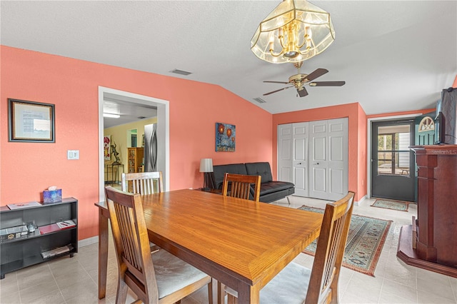 dining room featuring a textured ceiling, ceiling fan with notable chandelier, light tile patterned flooring, and vaulted ceiling