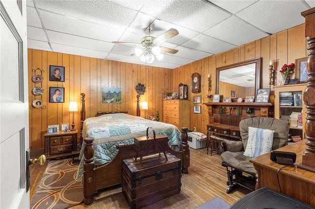 bedroom with wooden walls, a drop ceiling, hardwood / wood-style flooring, and ceiling fan