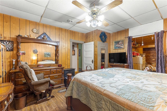 bedroom with hardwood / wood-style flooring, ceiling fan, wooden walls, and a paneled ceiling