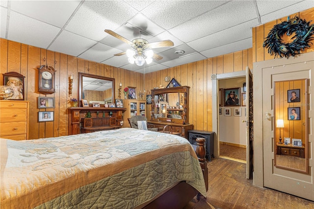 bedroom featuring ceiling fan, wood-type flooring, wood walls, and a paneled ceiling