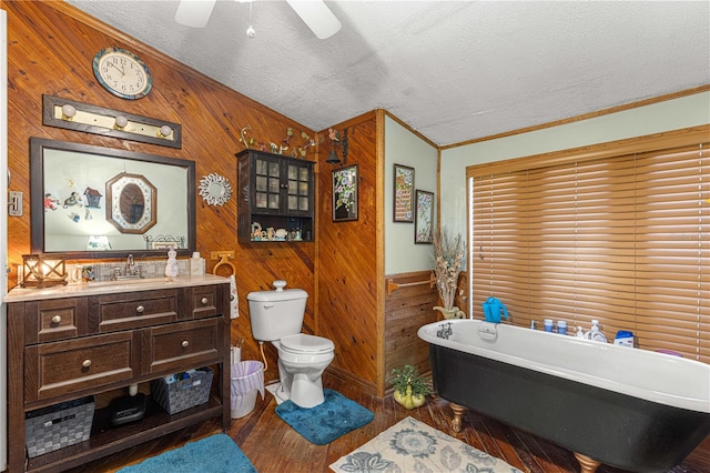 bathroom featuring a tub, a textured ceiling, hardwood / wood-style floors, wooden walls, and toilet