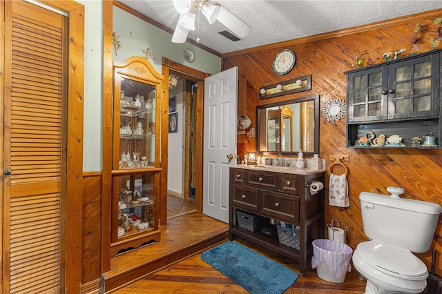 bathroom featuring toilet, wood walls, hardwood / wood-style flooring, vanity, and ceiling fan