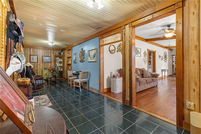 living room with dark wood-type flooring, wood walls, and ceiling fan