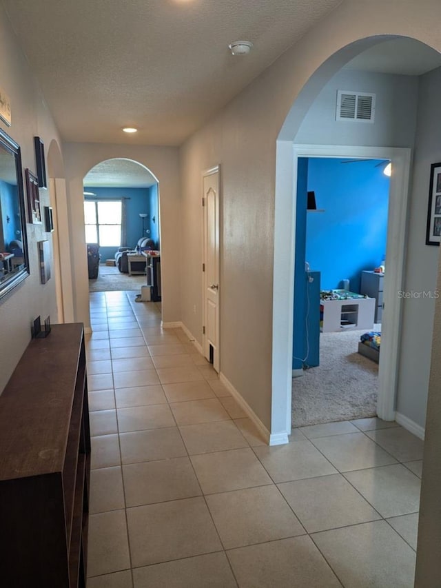 hall with a textured ceiling and light tile patterned floors