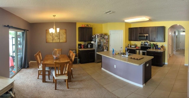 kitchen with a textured ceiling, an island with sink, light tile patterned flooring, appliances with stainless steel finishes, and decorative light fixtures