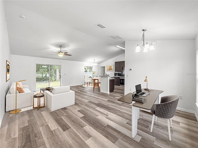 living room featuring vaulted ceiling, ceiling fan with notable chandelier, and light hardwood / wood-style flooring