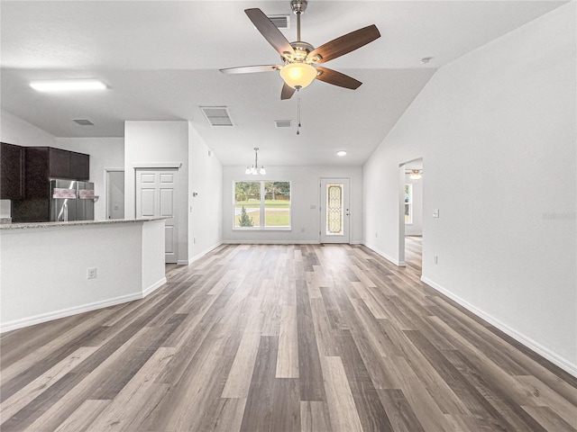 unfurnished living room featuring ceiling fan with notable chandelier, hardwood / wood-style flooring, and vaulted ceiling