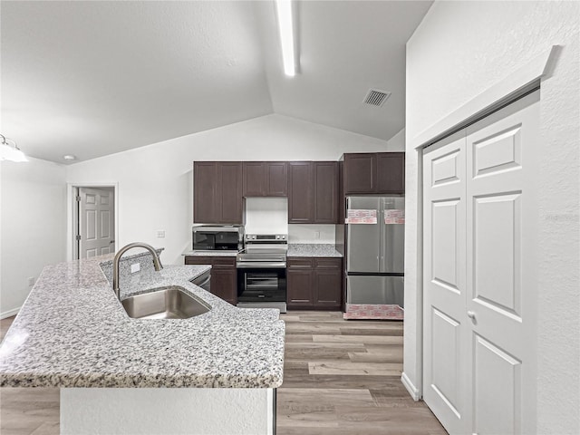 kitchen featuring a center island with sink, sink, appliances with stainless steel finishes, light hardwood / wood-style flooring, and vaulted ceiling