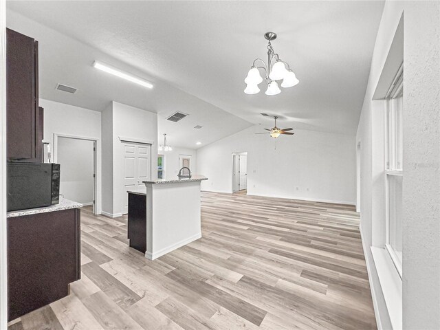 kitchen featuring ceiling fan with notable chandelier, a center island with sink, vaulted ceiling, dark brown cabinetry, and light hardwood / wood-style flooring