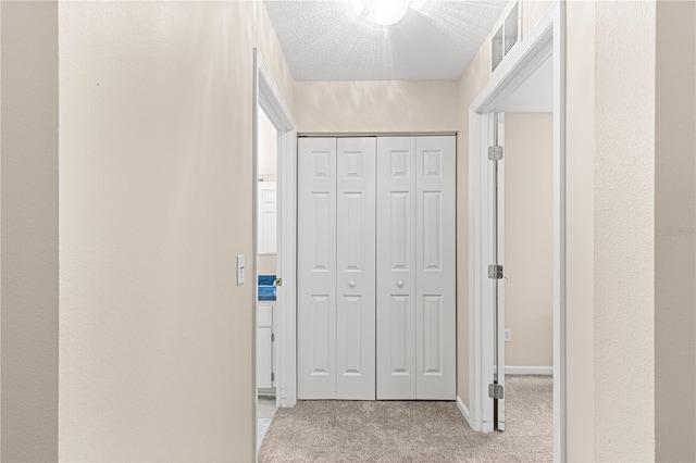 hall featuring a textured ceiling and light carpet