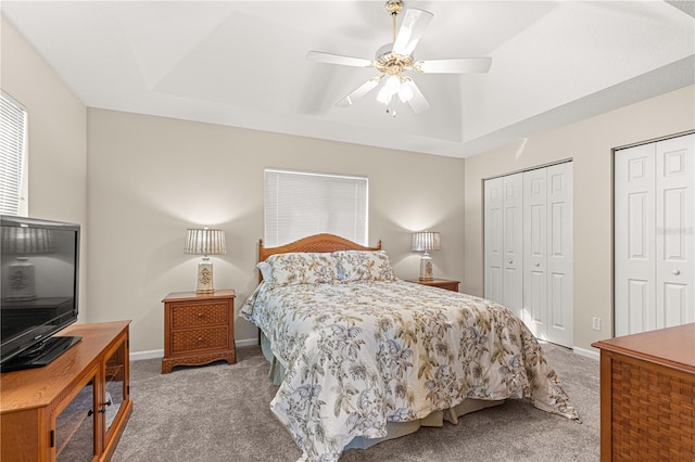 carpeted bedroom with ceiling fan, a raised ceiling, and two closets