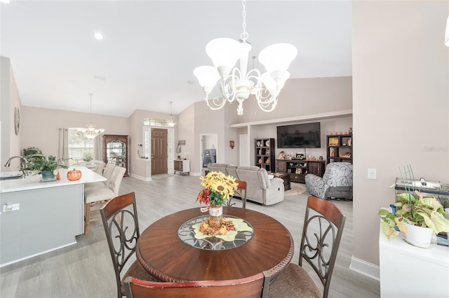 dining space featuring light hardwood / wood-style floors, lofted ceiling, sink, and an inviting chandelier